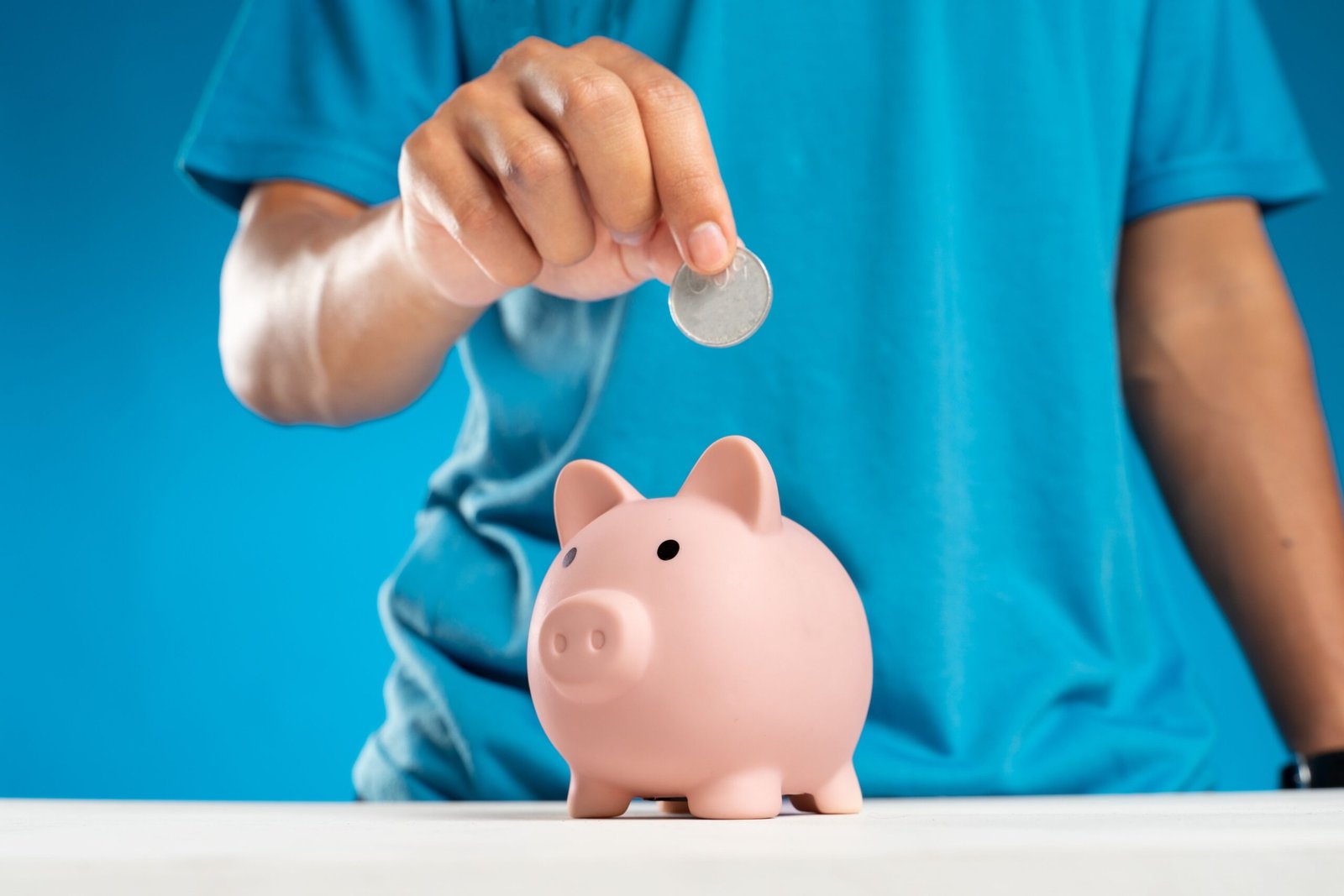 Hand dropping a coin into a piggy bank as capital-based passive income